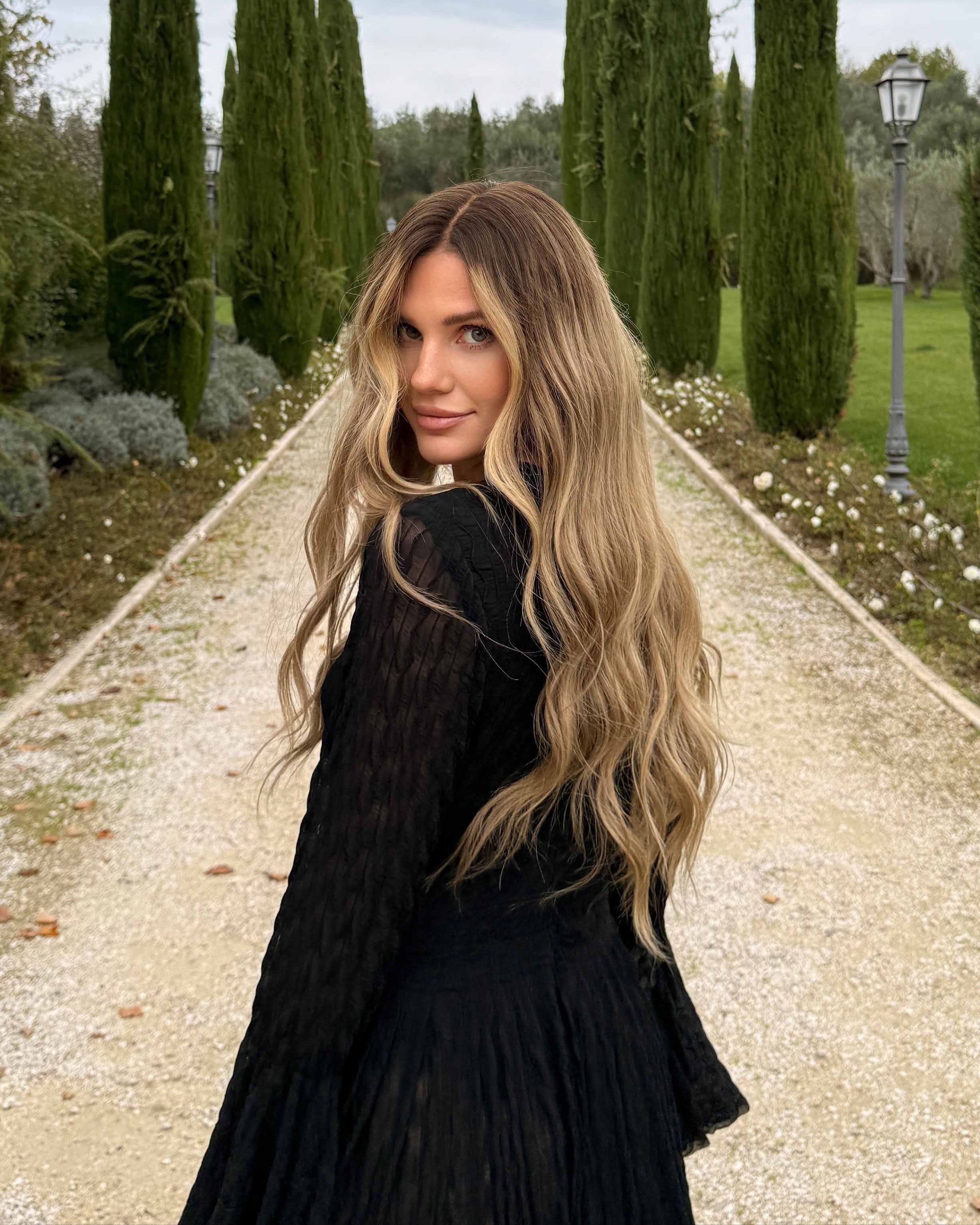 Woman wearing a long BHBD wig with dark blonde roots that transitions into slightly lighter lengths.